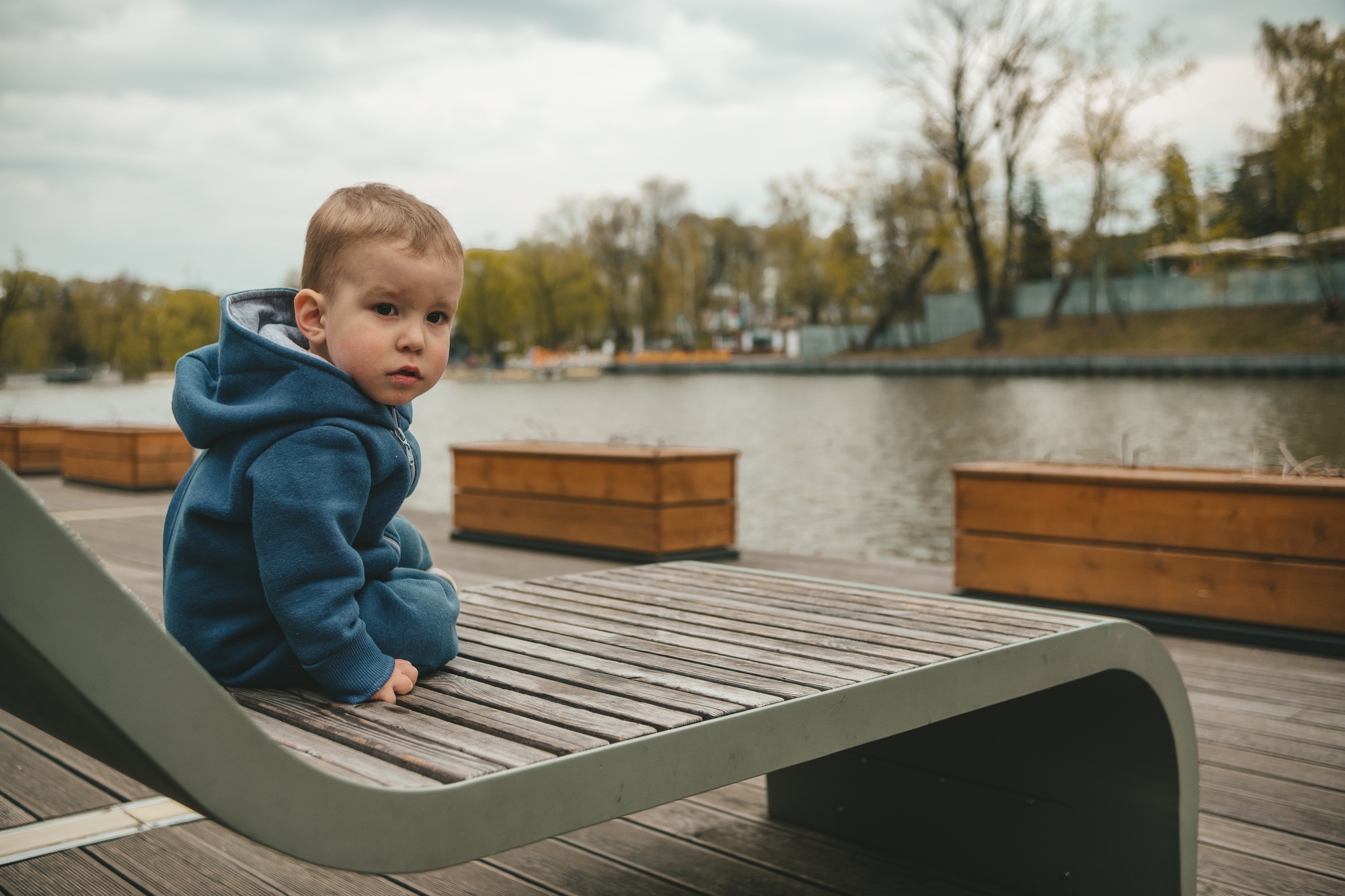 child is sitting on a deck chair on the river bank in spring